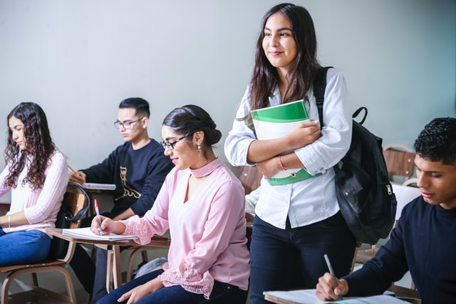 Image shows students in classroom. One student is standing and smiling.